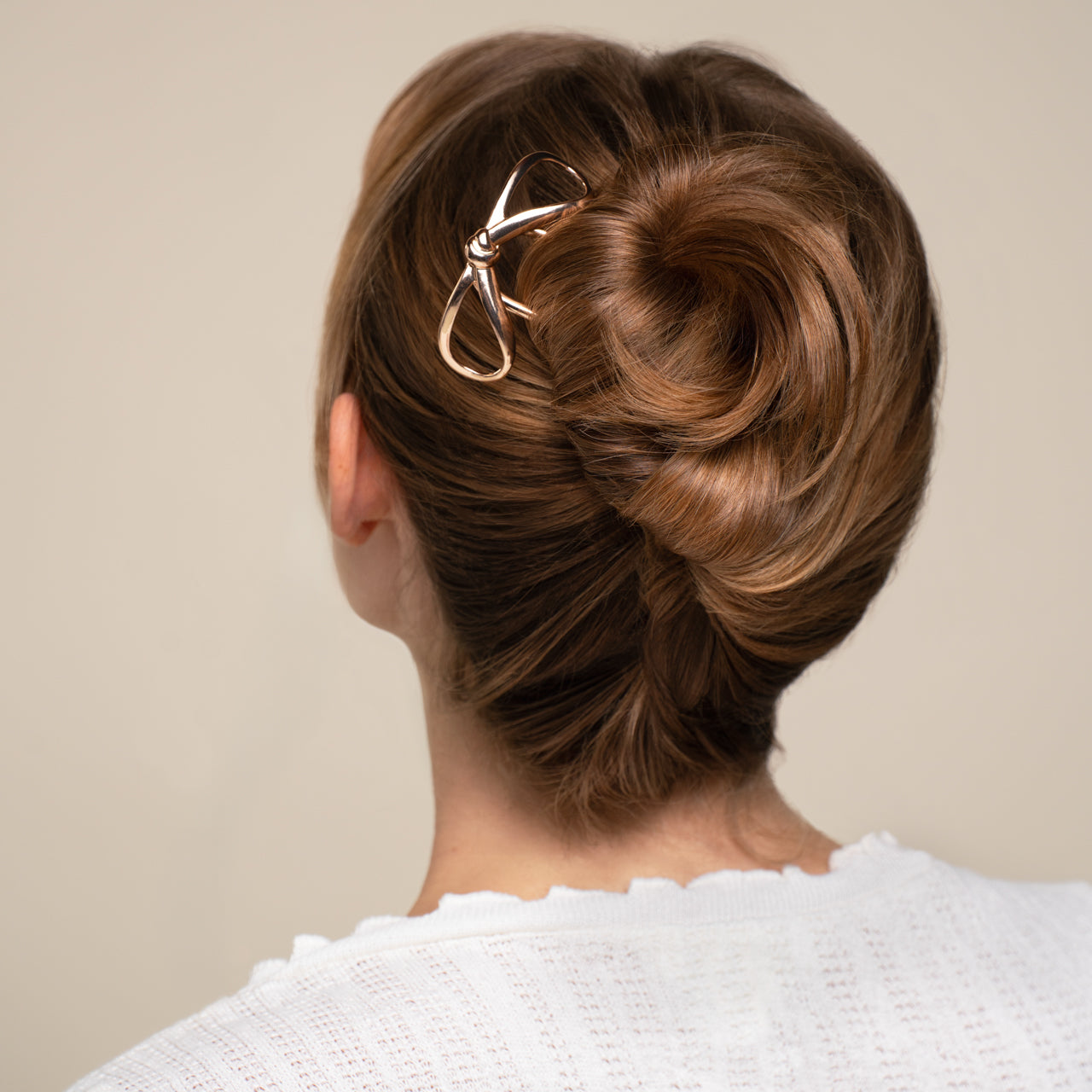 Woman with styled hair bun wearing a white sweater against a beige background
