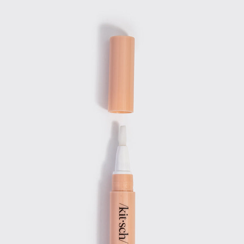 KITSCH Nourishing Nail & Cuticle Oil - Honey & Milk — top-down view of the uncapped peach pen with white brush tip and cap above it on a white background — support stronger, healthier-looking nails — brush oil onto each cuticle and around the nail