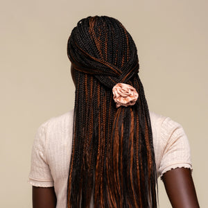 Person with microbraids styled with the Terracotta Rosette Ruched Satin Scrunchie on a plain beige background