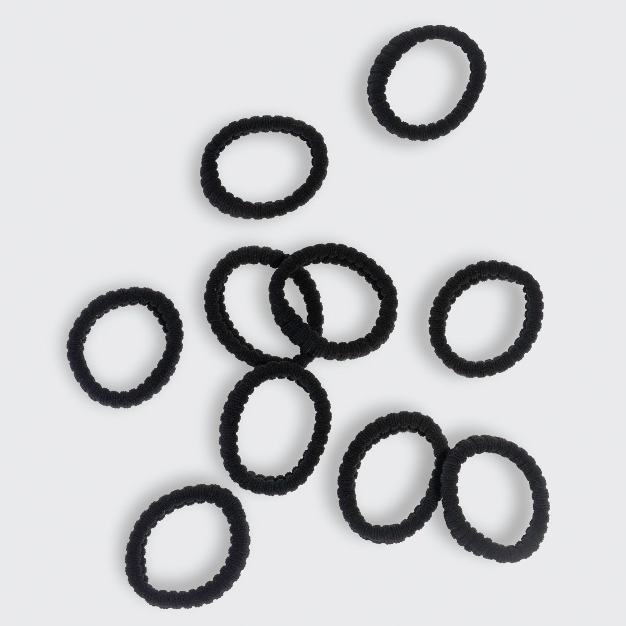 Kitsch black ribbed hair ties scattered on a light gray background