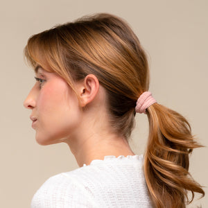 Woman with a kitsch blush ribbed elastic ponytail wearing a white sweater against a beige background