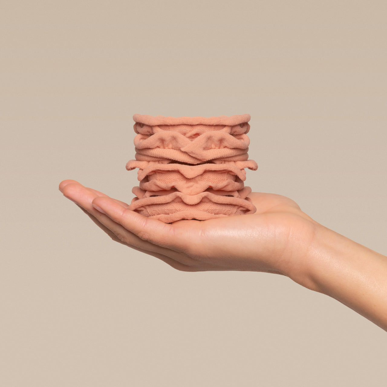 Stack of kitsch terracotta petal hair elastics in a hand against a beige plain background